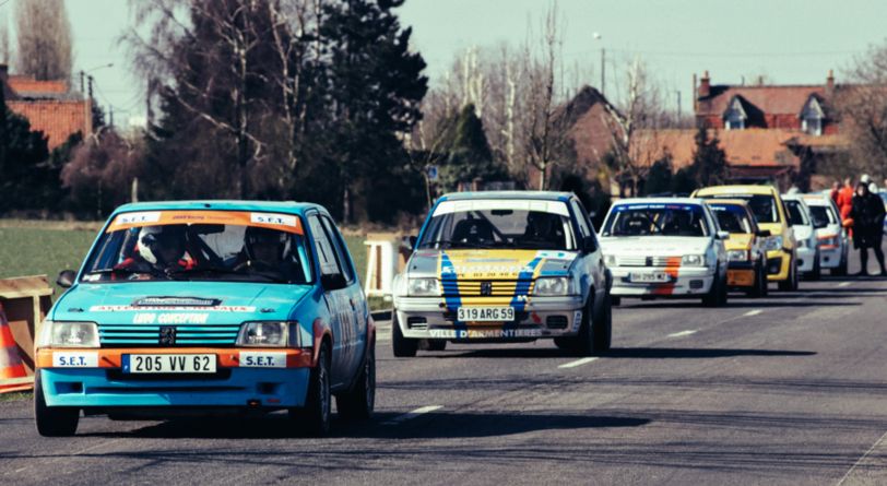 Des voitures de course (lors d'un rallye) en file indienne sur une route