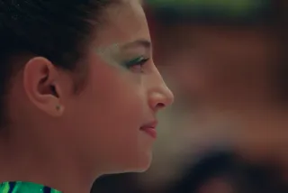 Le visage d'une fille en gros plan, de profil. Elle a les yeux légèrement maquillés en vert. Elle regarde vers la droite et semble concentrée.