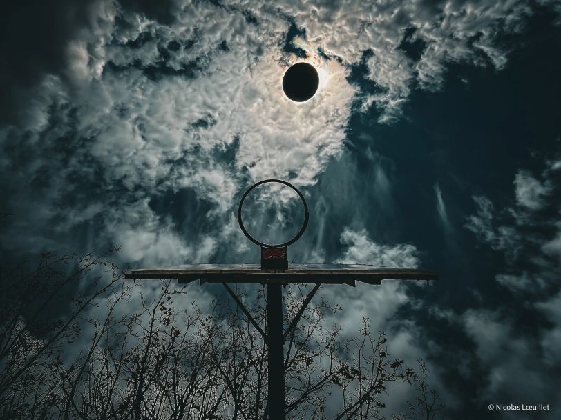 Un panier de basket pris par dessous. Un ballon passe juste devant le soleil au même moment.
