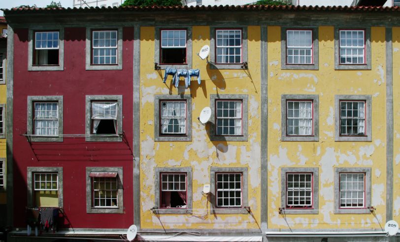 Trois façades d'immeubles. Celle de gauche est rouge, les deux autres sont jaunes. Il y a des paraboles et du linge accroché.