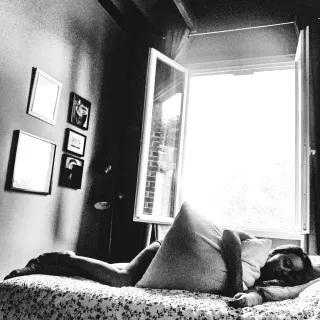 Une personne allongée sur un lit. La fenêtre derrière elle est grande ouverte