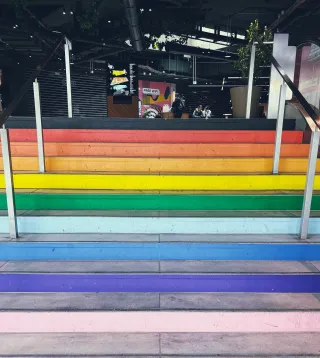 Un escalier dans un bâtiment. Chaque marche est colorée aux couleurs de l'arc-en-ciel