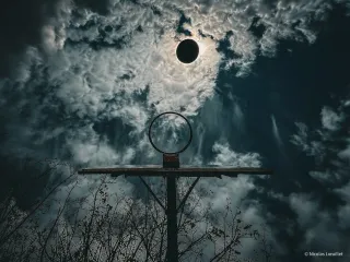 Un panier de basket pris par dessous. Un ballon passe juste devant le soleil au même moment.