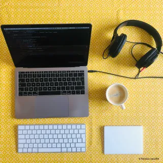 Photo du dessus d'un ordinateur, un casque audio, une tasse de café, un clavier et un trackpad. Tout est posé sur une table avec une nappe jaune.