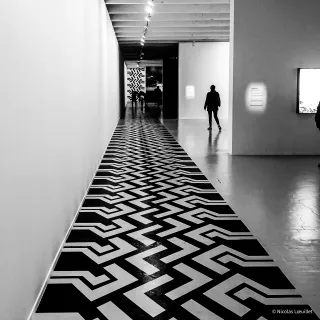Un couloir en noir et blanc. Au sol, des formes géométriques.