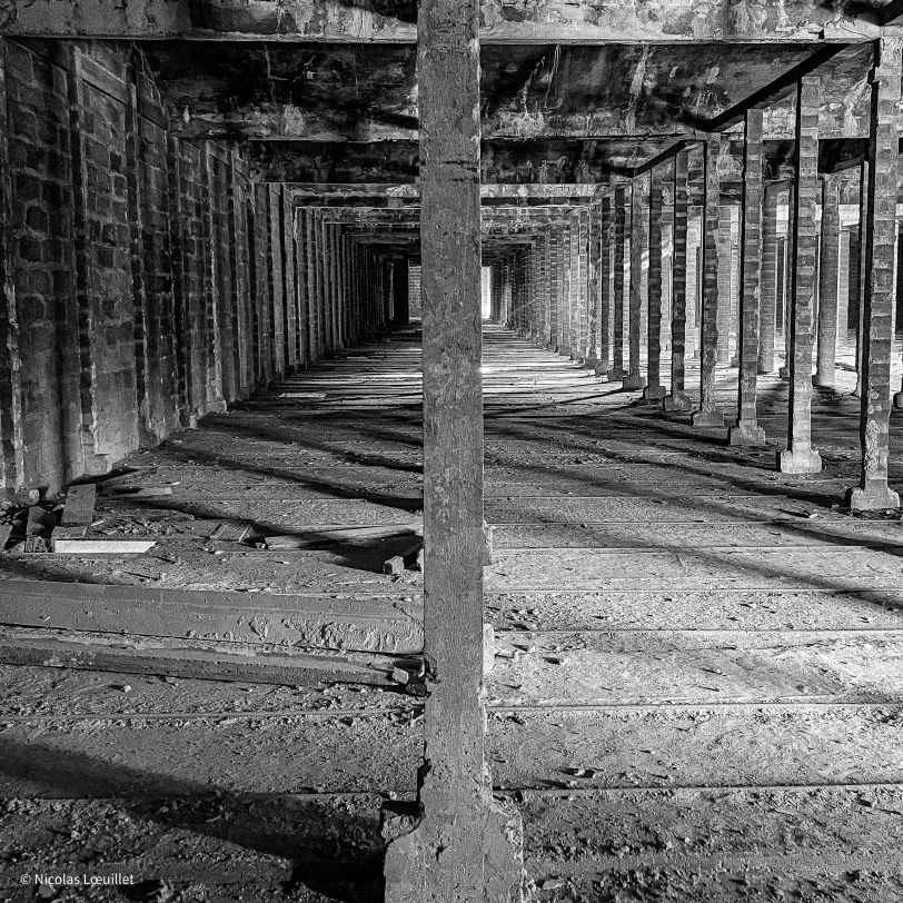 Un bâtiment abandonné. Au premier plan et au milieu de la photo, un poteau. En arrière-plan, les autres poteaux qui soutiennent la toiture.