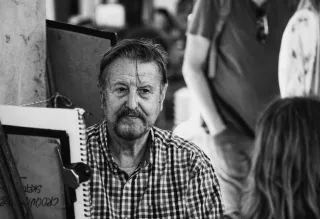 Photo en noir et blanc d'un homme dessinant le portrait d'une autre personne, que l'on devine au premier plan.