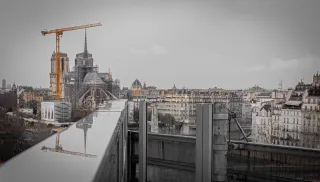 En arrière plan, on aperçoit Notre-Dame de Paris. En premier plan, on voit le reflet de Notre-Dame dans de l'eau stagnante sur une barrière.