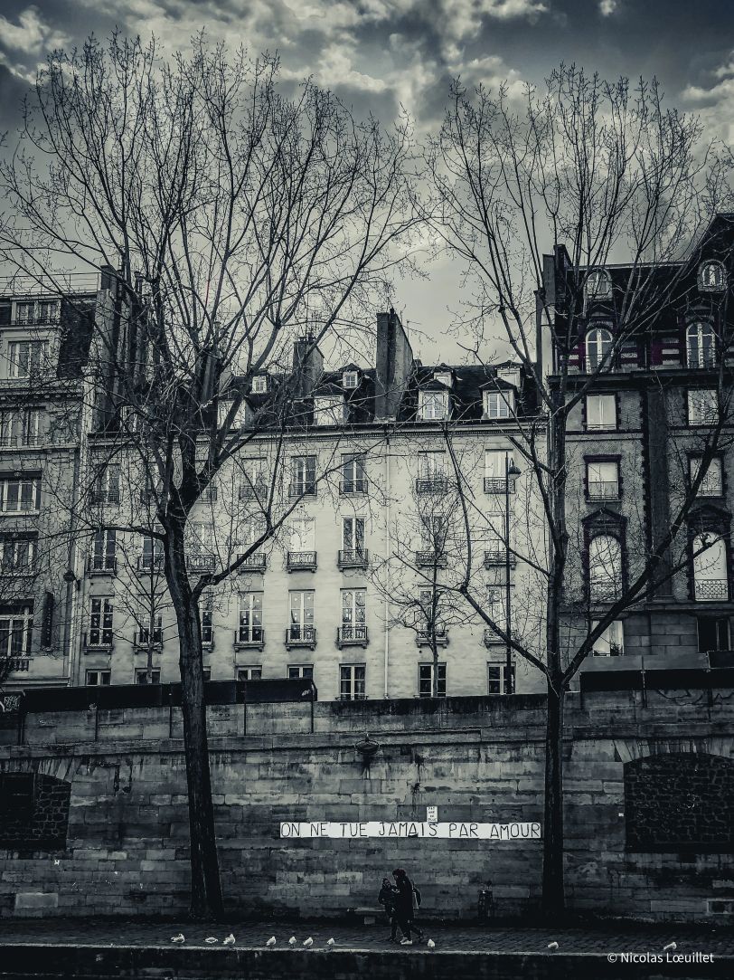La phrase « On ne tue jamais par amour » collée sur un mur. Derrière, des habitations.