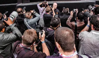 Photo prise durant un concert. Elle est cadrée sur un agent de sécurité, qui est entourée d'une dizaine de photographes qui prennent en photo la scène (qu'on ne voit pas).